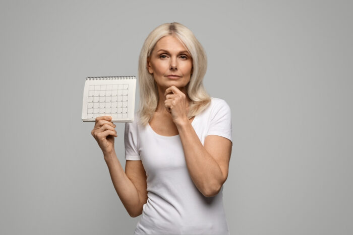Mulher madura segurando um calendário e pensando.