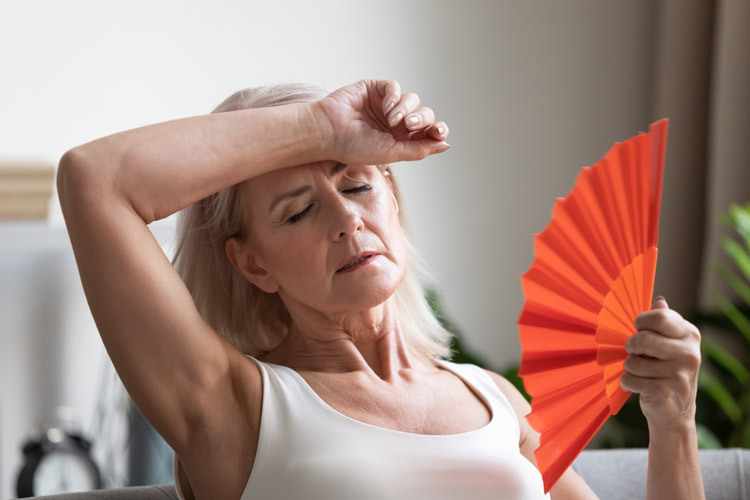mulher com calor utilizando um leque para representar menopausa devido falência ovariana precoce