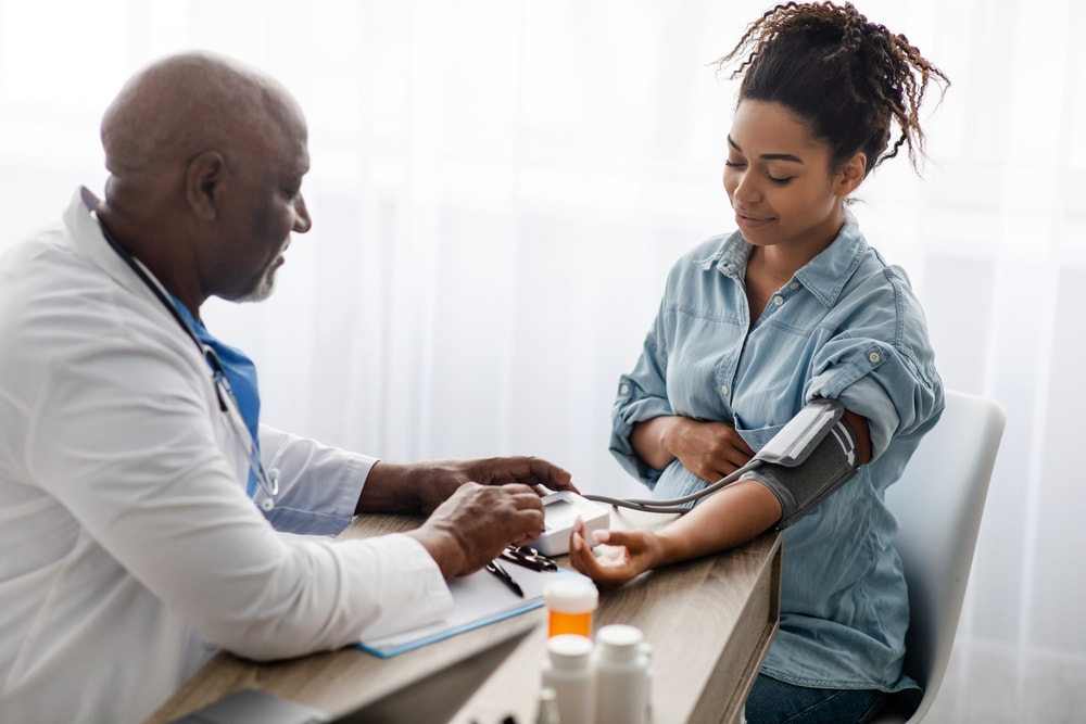 Médico negro utilizando o aparelho para medir a pressão de uma mulher negra que está grávida.