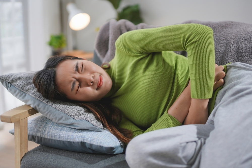 Mulher deitada em sofá com dor abdominal.