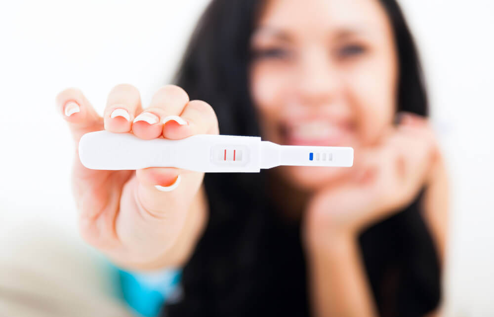 Mulher segurando um teste de gravidez positivo e sorrindo