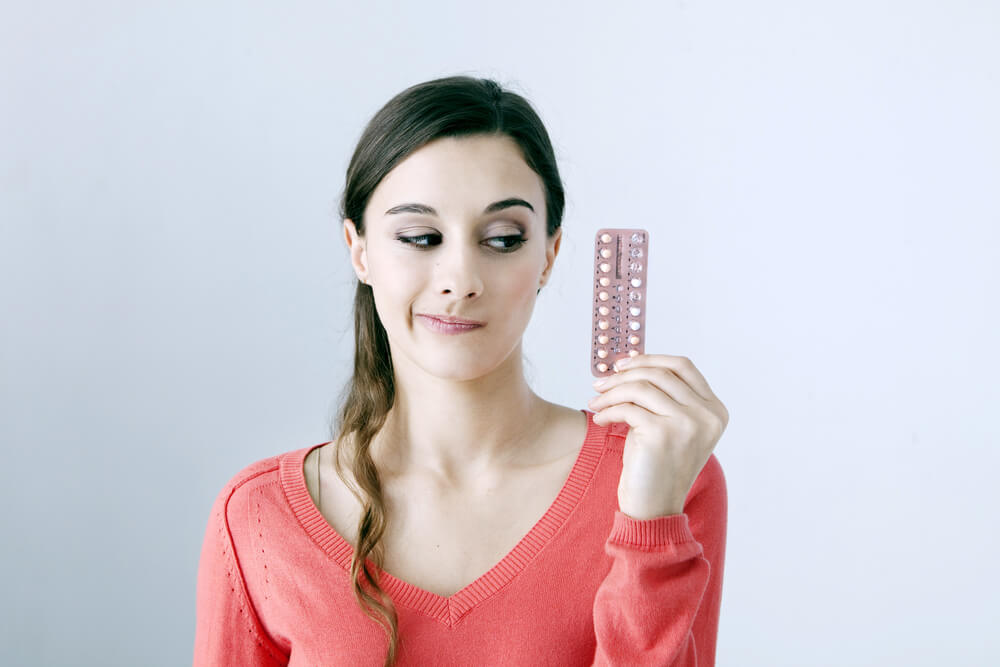 Mulher olhando para uma cartela de anticoncepcionais.