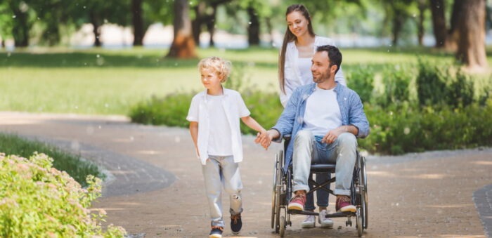 pai cadeirante segurando a mão de seu filho em uma caminhada no parque