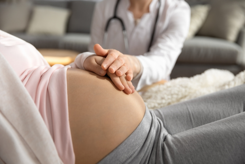 Mulher grávida e médica com as mãos em cima de barriga.