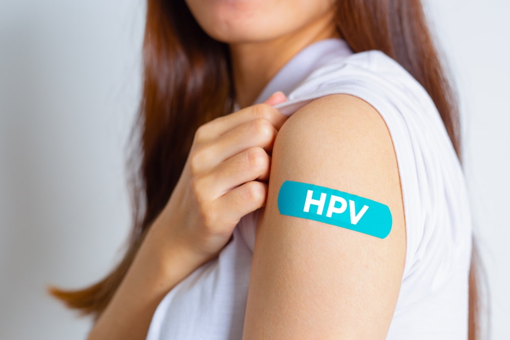 mulher com braço à mostra com band-aid escrito "HPV" como sinalização para prevenir o HPV