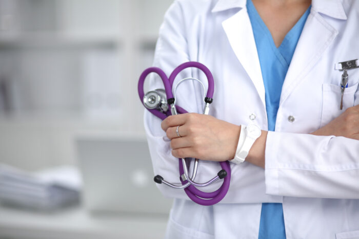 Médico de braços cruzados segurando um estetoscópio.