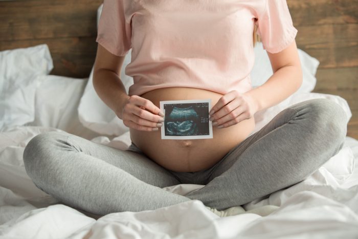 Mulher segura ultrassom em frente a barriga depois de seguir todos os cuidados na gravidez