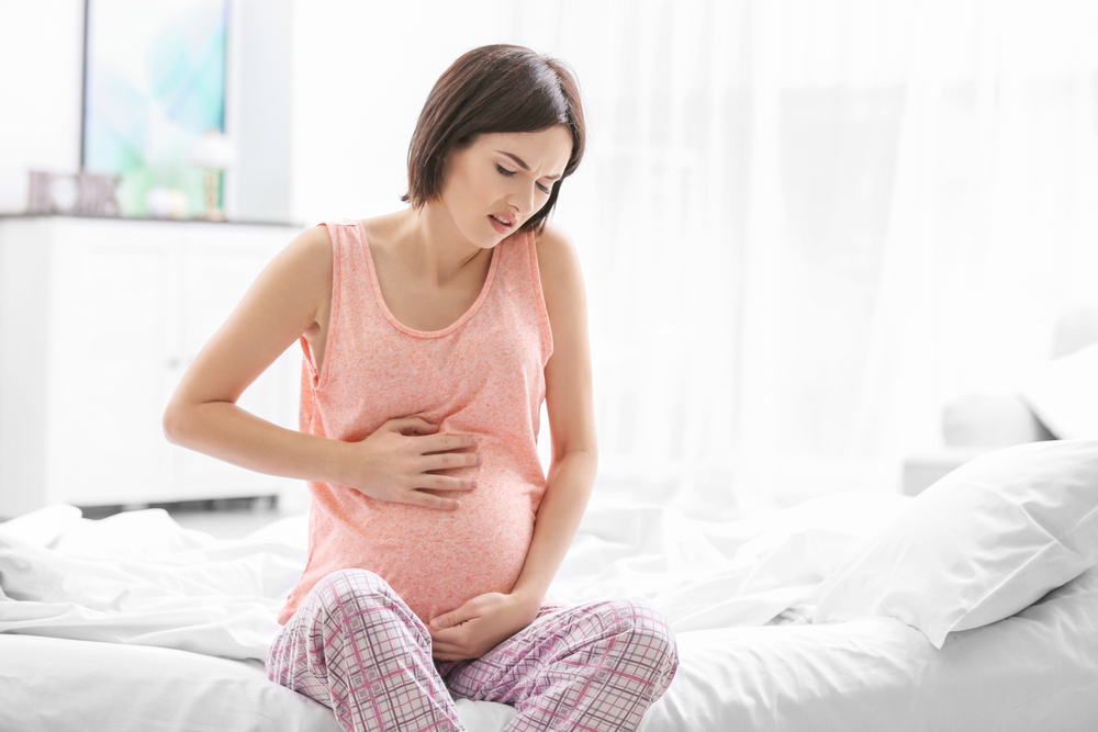 Mulher com mãos na barriga enquanto sente dor de pré-eclâmpsia