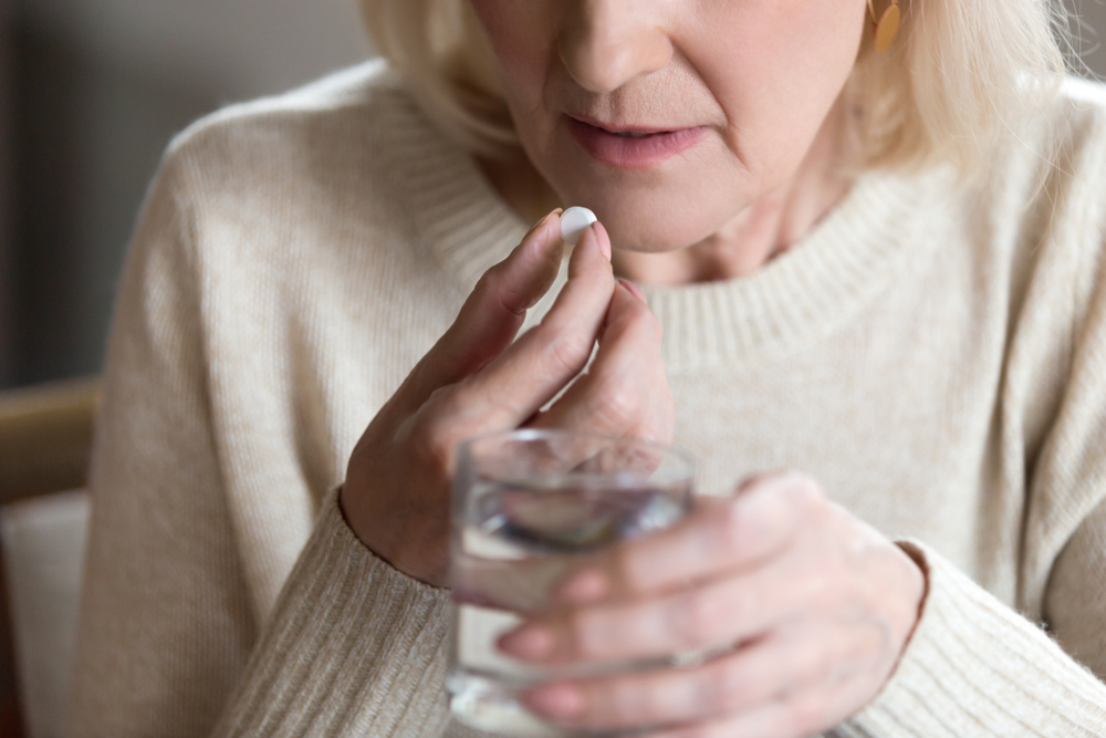 Mulher idosa toma comprimidos para a reposição hormonal na menopausa