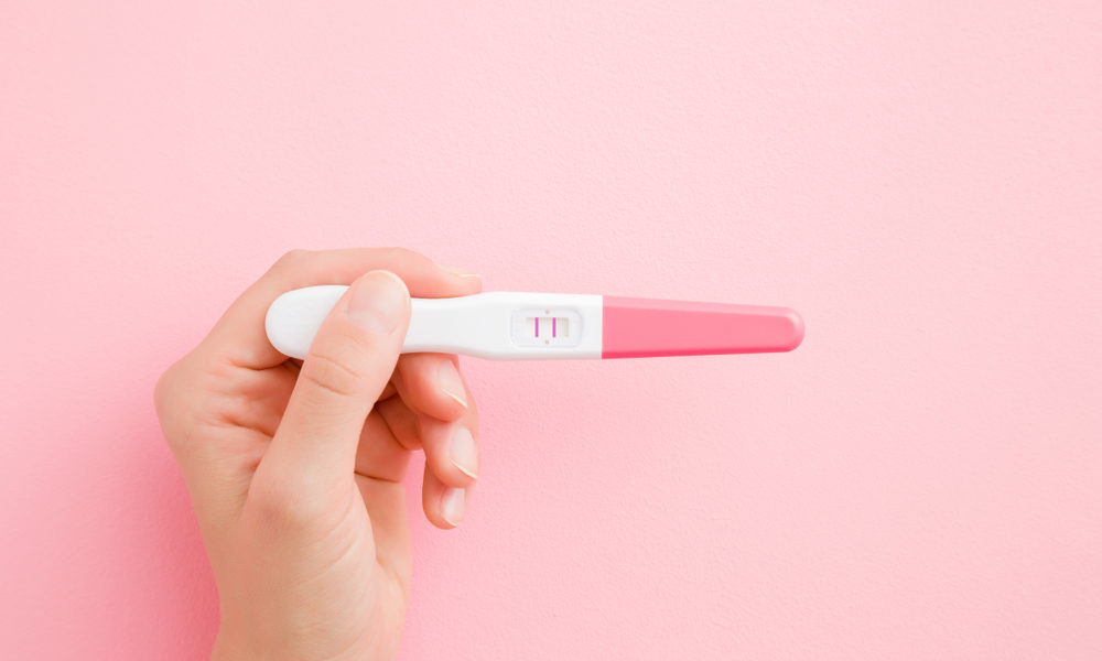 Mão segurando teste de gravidez com fundo rosa claro