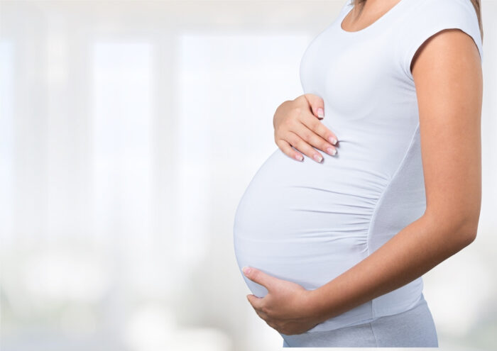 Mulher branca grávida com as mãos posicionadas na barriga.