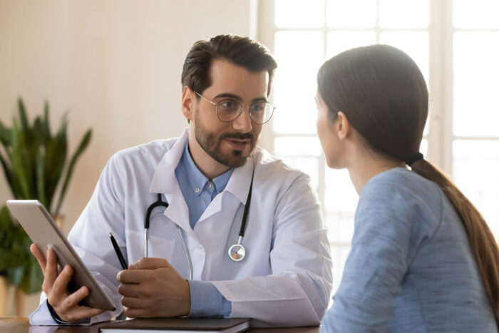 Mulher branca em consulta com um médico branco. Os dois estão conversando, talvez falando sobre desequilíbrio hormonal da paciente.