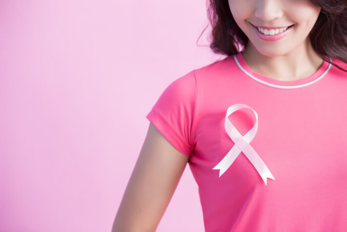 imagem de mulher vestindo uma camiseta rosa com laço no peito para representar outubro rosa.