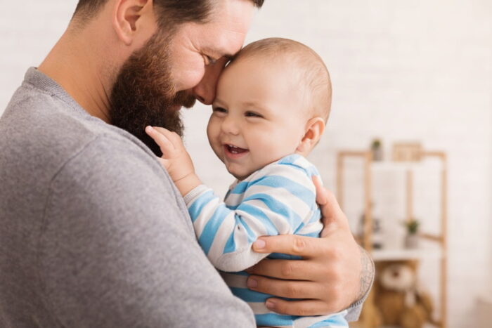 Homem com bebê no colo, os dois estão sorrindo