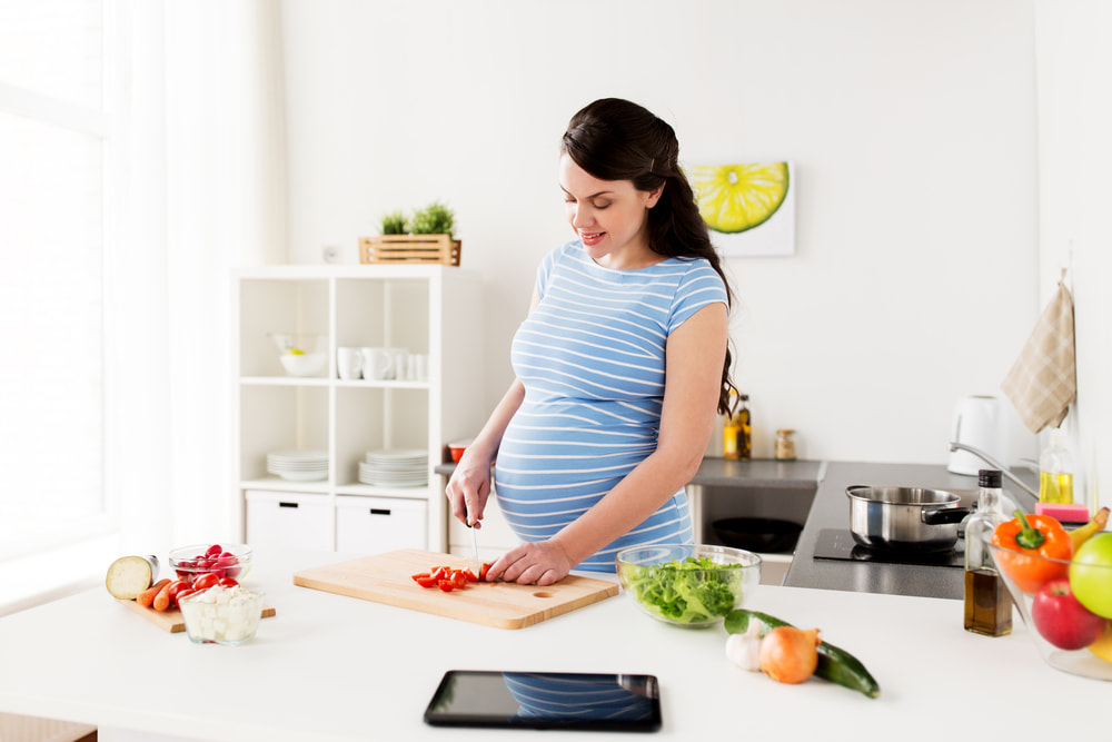 Mulher grávida cozinhando.