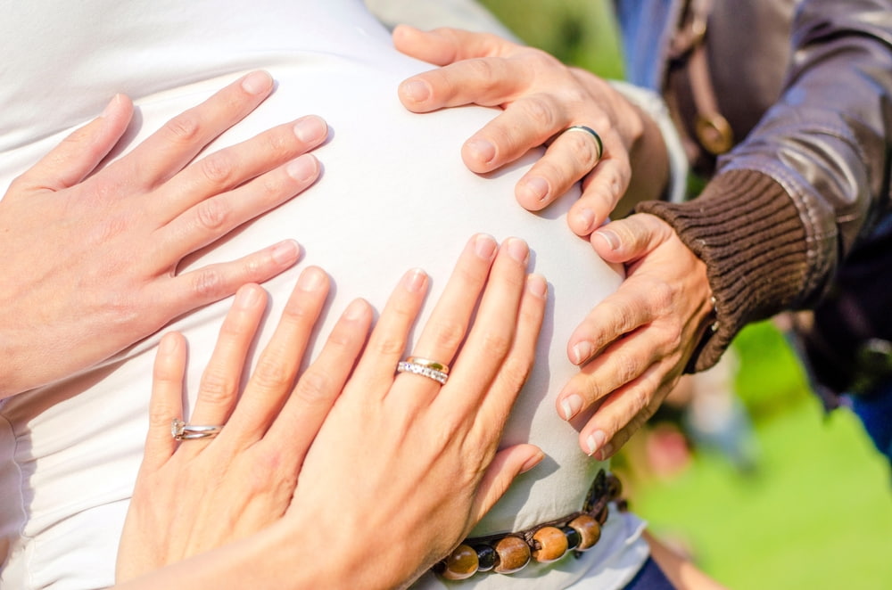 Mãos em cima de barriga de mulher grávida.