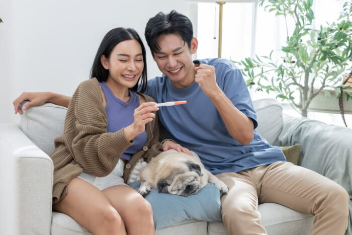 Casal feliz com teste de gravidez. Também há um cachorro ao lado deles.