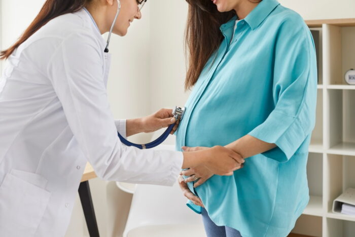 Médica examinando barriga de mulher grávida.