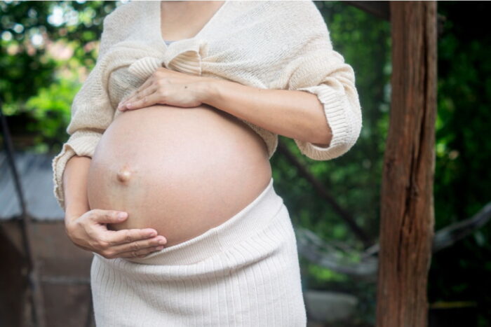 Mulher grávida com as mãos posicionadas ao redor da barriga.