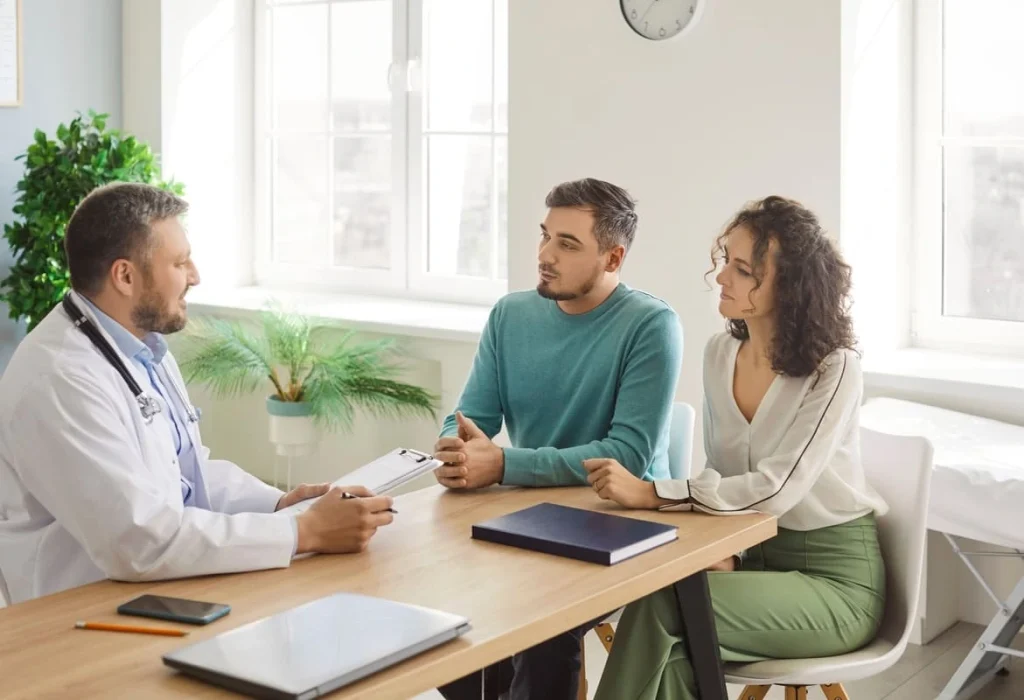 Casal em consulta com médico recebendo orientações sobre como se preparar para FIV.
