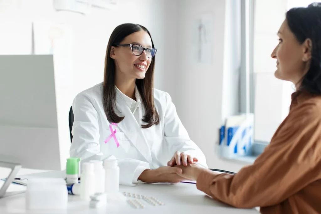 Médica com fita rosa segurando a mão da paciente representando a questão se quem tem câncer pode engravidar.