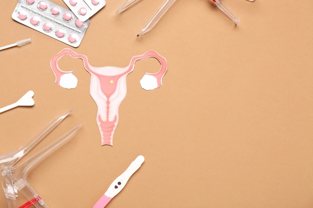 Útero de papel com espéculos ginecológicos, pílulas e instrumentos para exame de Papanicolau sobre fundo marrom.